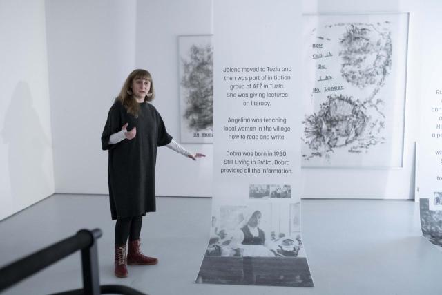Artist standing with gestures of explaining the written content of posters hanging from the ceiling