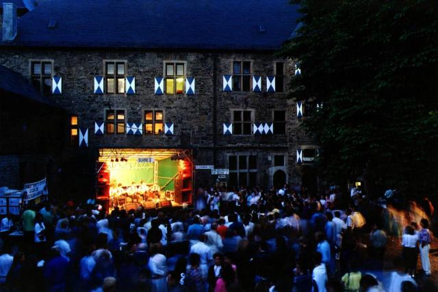 people at a festival. 4 people are playing instruments and singing and the others are listening and dancing.