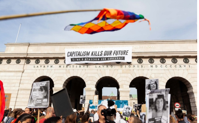 on Top of a Facade we read "Capitalism kills our future" and a Andean colourful flag