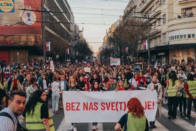A protest on a street full of people. 4 young women held a banner.