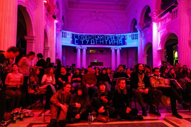 Students are sitting on a salon. Colorful lights are displayed on the room. 