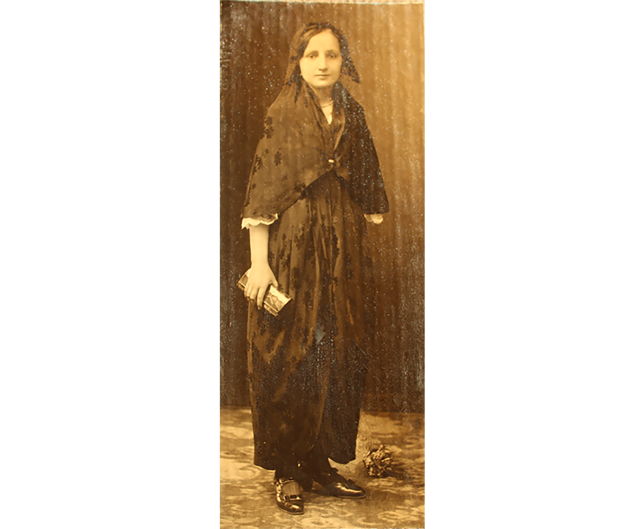 female body holding a hand purse, dressed in black and looking at the camera.