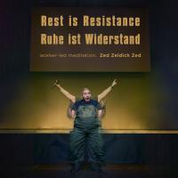 a man lifting up a sign board that says "rest is resistance"