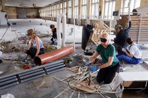 Five people interacting with construction materials and tools with their eyes covered.