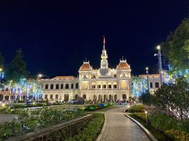 Park mit viel Vegetation und im Hintergrund ein mit bunten Lichtern beleuchtetes Gebäude.